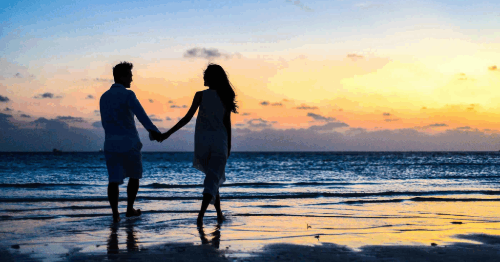 Romantic Couple holding hands walking on beach at sunset. Relationship goals, affection and travel concept.