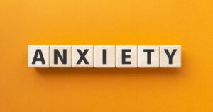 Wooden letter tiles spell the word anxiety on an orange background.