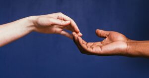 Two hands reaching toward each other against a blue background, symbolizing connection and support.