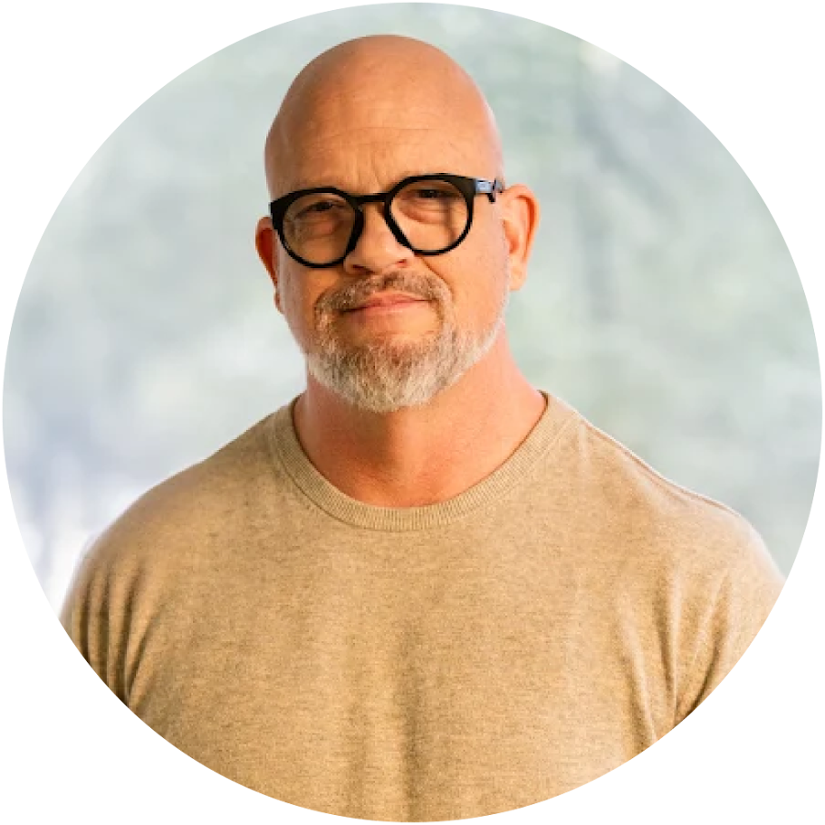 image-2-1png - Lonestar Mental Health Portrait of a smiling, bald man with glasses and a gray beard wearing a beige sweater, with a soft blurred background.